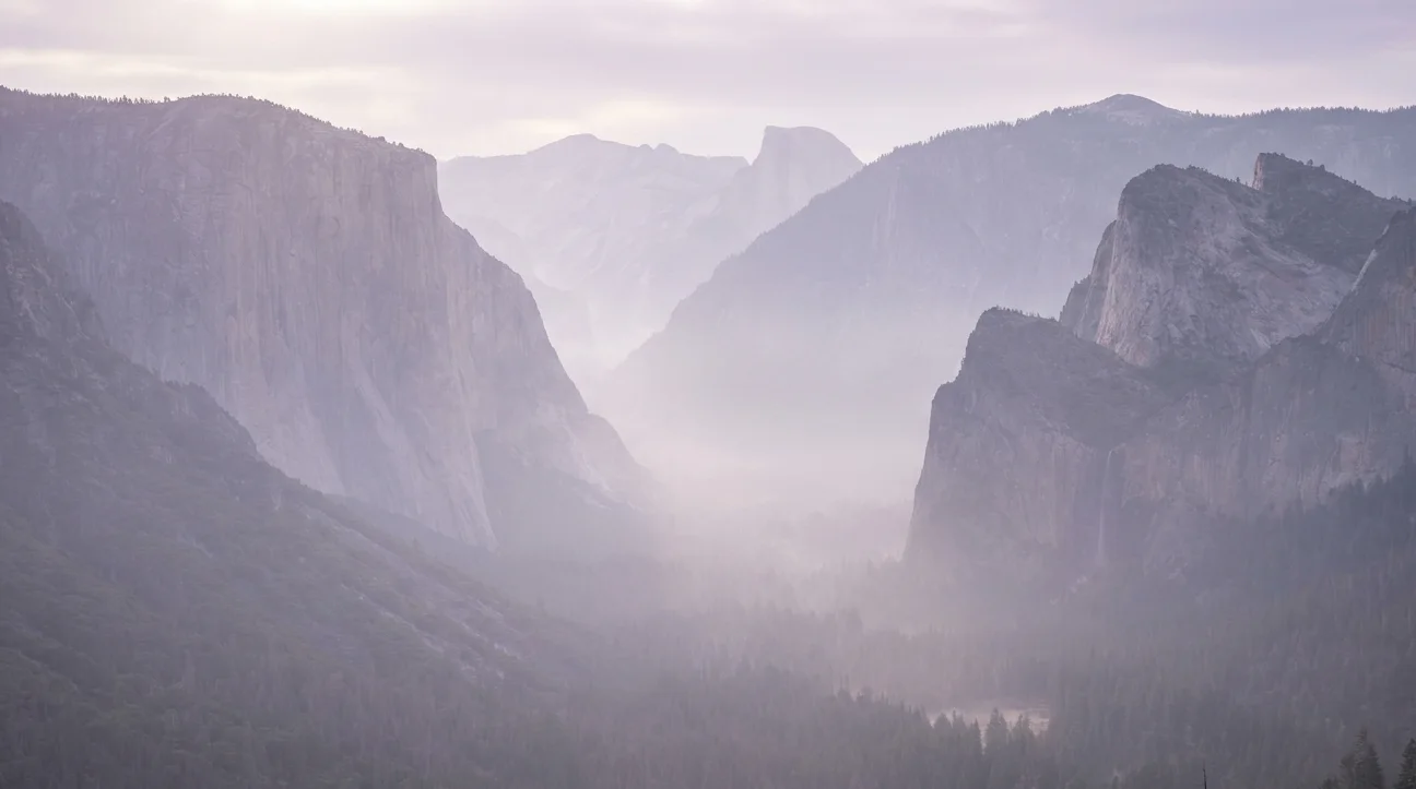 Misty Yosemite valley at dusk with granite cliffs fading into fog